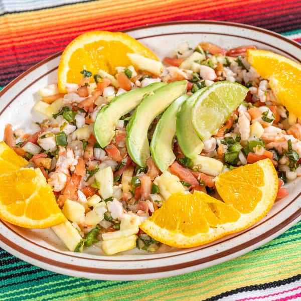 Chula on Broadway's shrimp ceviche with avocado, lime, and orange slices on a colorful striped tablecloth.