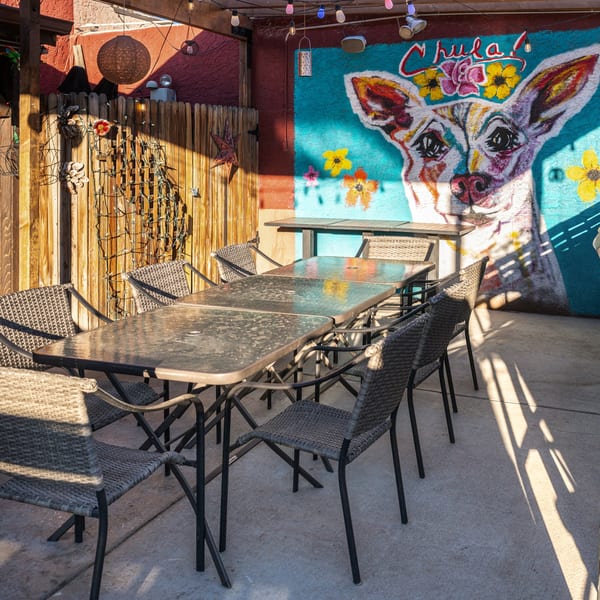 Outdoor patio at Chula on Broadway with tables, chairs, and a colorful mural of a dog.