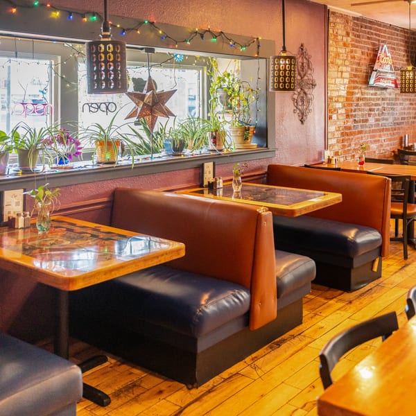 Interior of Chula on Broadway, a Mexican restaurant, with booths, wooden tables, and plants by the window.
