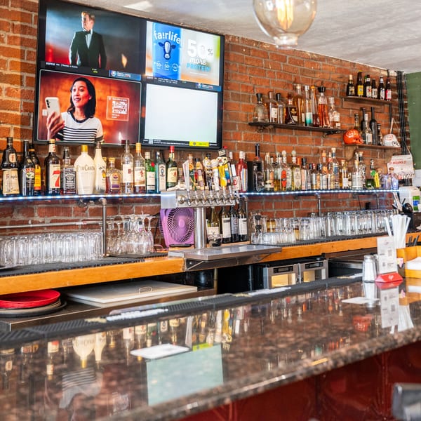 A well-stocked bar at Chula on Broadway, with liquor bottles, beer taps, and TVs showing sports.