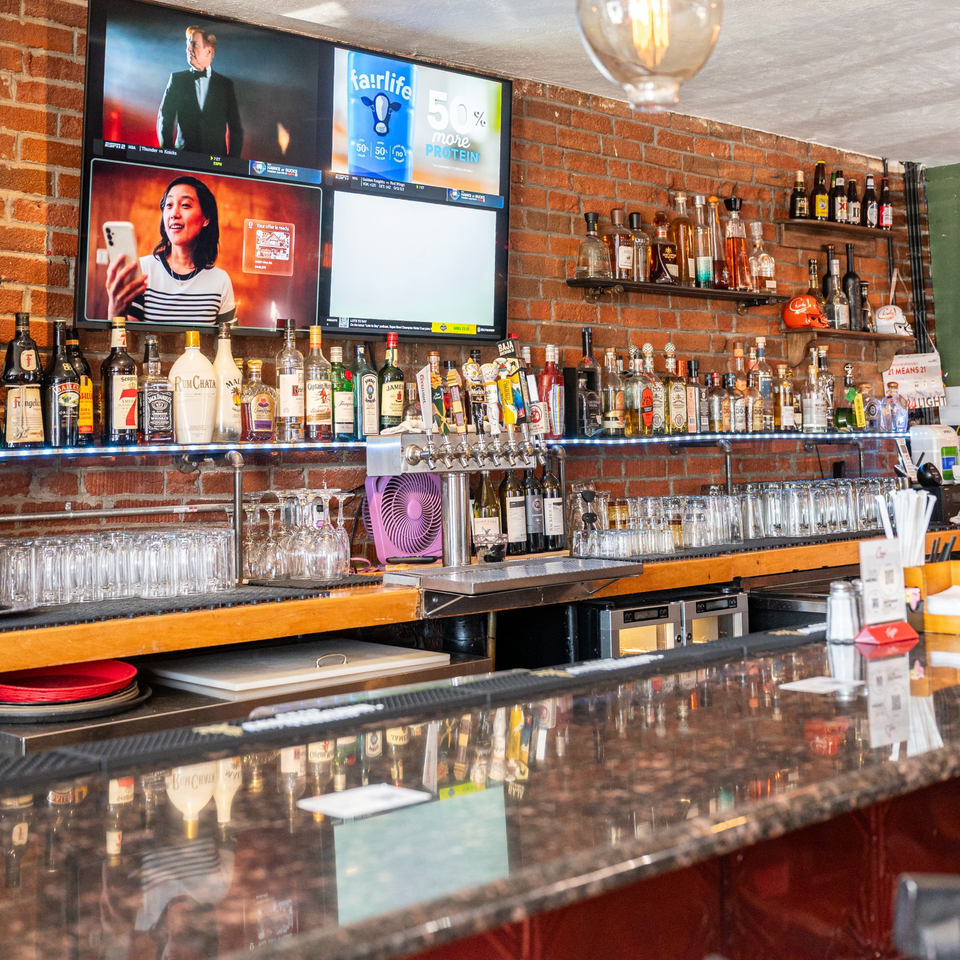 A well-stocked bar at Chula on Broadway, with liquor bottles, beer taps, and TVs showing sports.